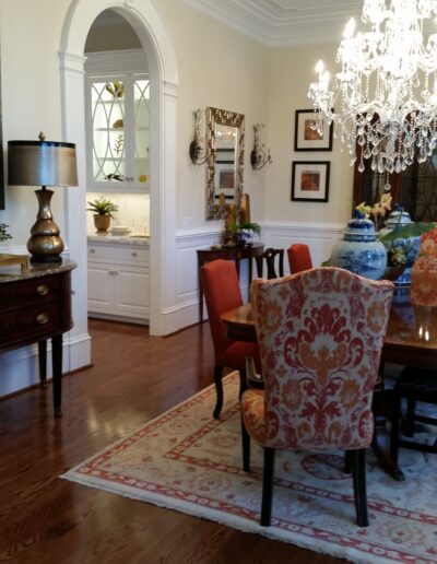 Elegant dining room with wooden floor, chandelier, patterned chairs, round table, and decorative items; arched doorway leads to a bright adjoining room.