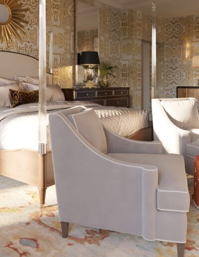 A spacious bedroom with a large bed, two gray armchairs, an orange ottoman, patterned wallpaper, and elegant wooden furniture.