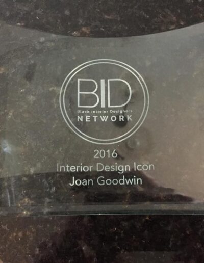 A glass award plaque reads "BID Network 2016 Interior Design Icon Joan Goodwin" on a dark marble surface.